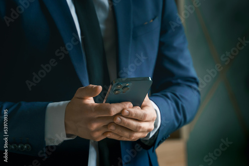 Businessman in suit with mobile phone in hands. Man typing message, using social net. Checking news. Making business meeting. Modern office.General manager,ceo.Calling to partner.Planning working day