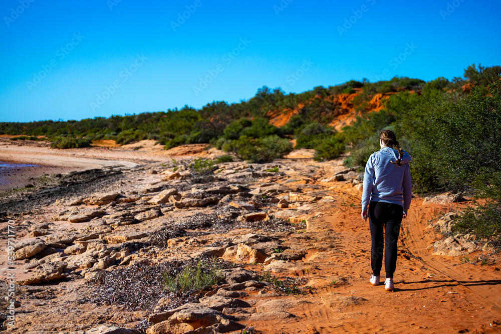 girl walks on red sand beach with red cliffs in the background, terra rosa in australia, holidays in western australia, francois peron national park