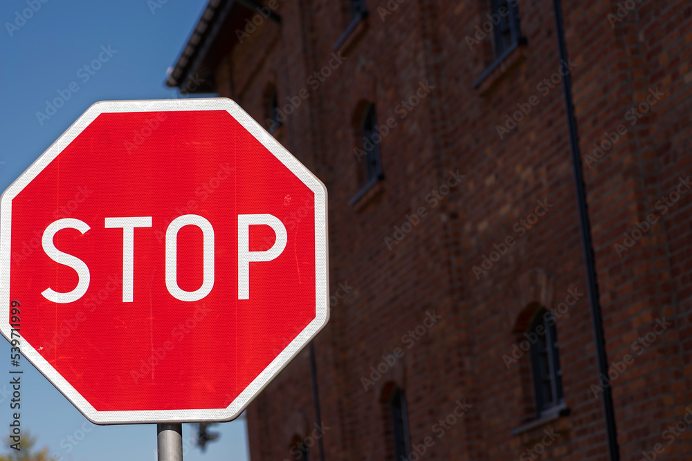 Ośmiokątny znak STOP ! Znak o wielokątnej tarczy i czerwonej barwie ( z białymi : napisem i oblamówką ) na tle budynku z czerwonej cegły . - obrazy, fototapety, plakaty 