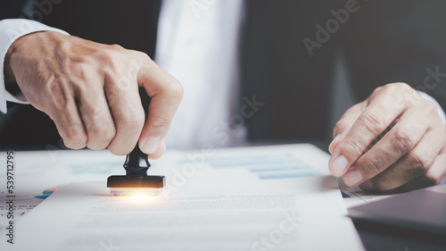 A young executive is stamping on documents for a business contract. Transaction and document management concepts include negotiating corporate entities and filling out legal forms or agreements.