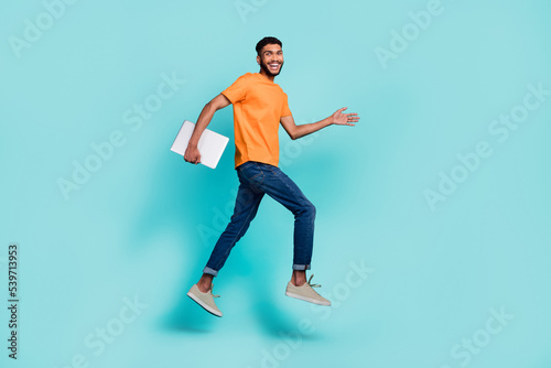 Full body profile portrait of carefree cheerful guy running jump hold netbook isolated on cyan color background