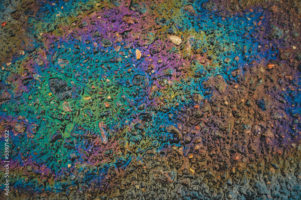 Oil stains on wet asphalt. Puddles are contaminated with multicolored streams of oil.