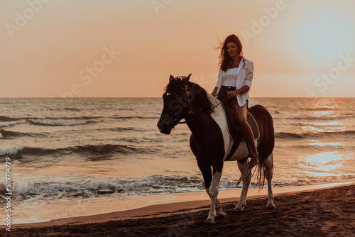 Woman in summer clothes enjoys riding a horse on a beautiful sandy beach at sunset. Selective focus 