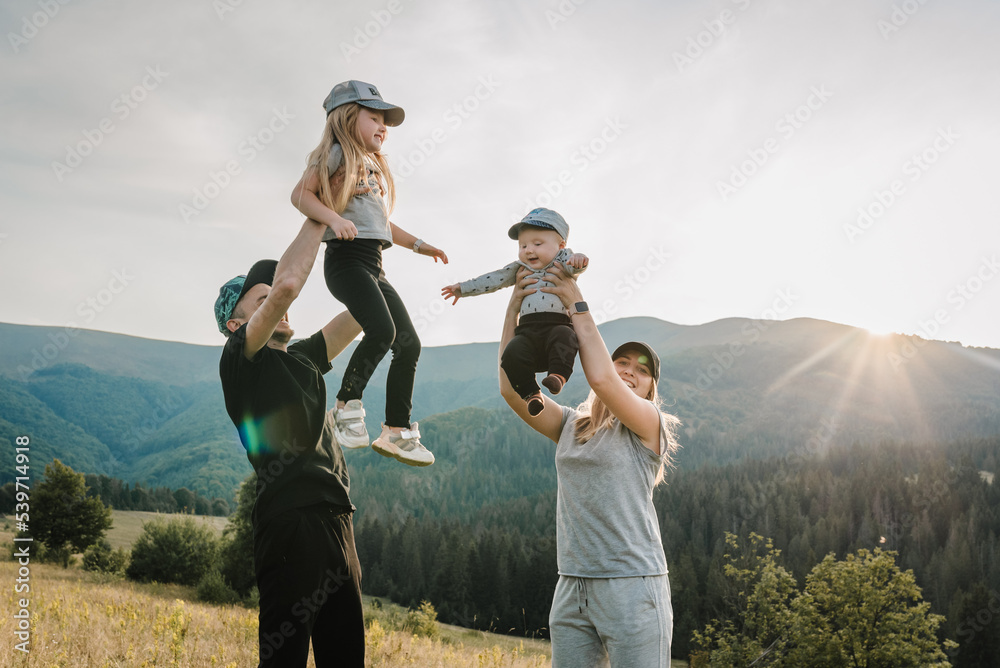 Parents hold in hands and throw up happy children into the sky. Mother, father, son and daughter walking in nature on an autumn day in mountains. Concept of family spending time together on vacation.