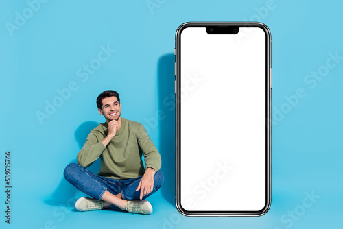 Full size photo of minded man sit floor hand chin look empty space isolated on blue color background