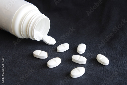 Botella de plàstico blanca con medicamento en pastillas para tratamientos de enfermedades volcadas sobre la mesa, forma un original diseño farmacèutico con fondo negro