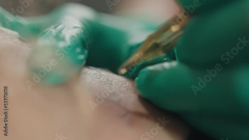 Close-up macro of tattooing process, master in gloves works with machine.