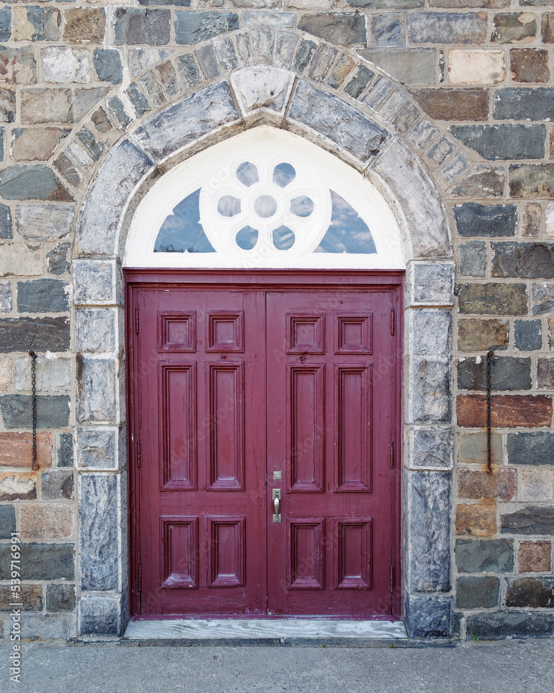 A dark red double door in the stone wall of an old building.