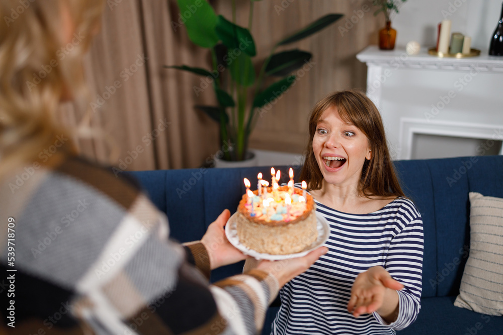 Happy birthday my sweetie. Woman gives a cake with candles to her daughter who sitting on the sofa Happy birthday my sweetie. Woman gives a cake with candles to her daughter who sitting on the sofa