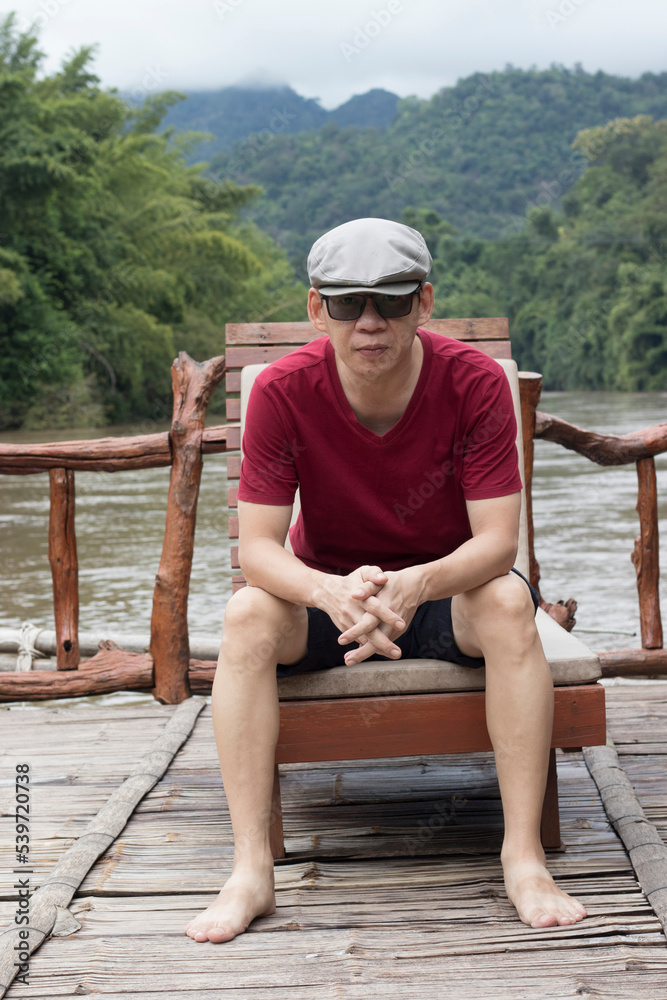 Portrait photo of an Asian man looking man with handsome having a nice time outdoors in a vacation forest by the River. relaxing, happy, and fun with a vacation.