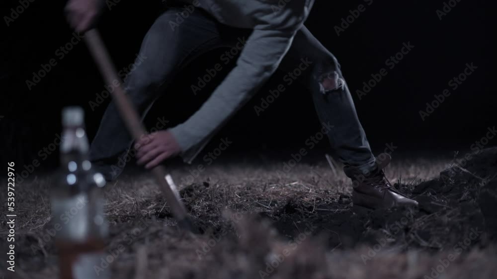 Criminal digs hole at night Young scary man digs hole in field. Close up of legs.