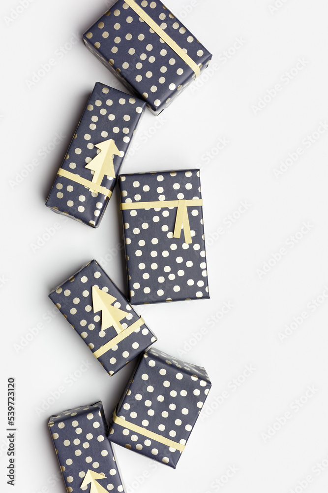 Obraz premium Christmas vertical poster, wrapped paper gift boxes on white fon, trendy packaging presents for holidays. DIY idea New Year gifts decorated cutting golden paper fir. Xmas frame background