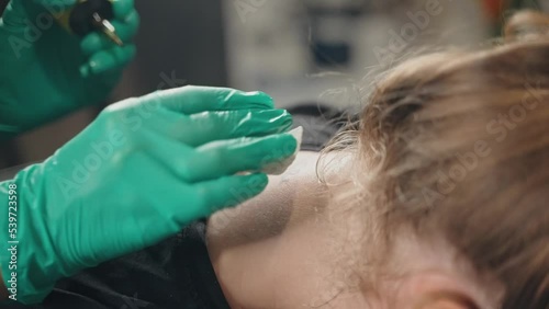 Master in gloves beats tattoo on neck client with machine according to sketch.