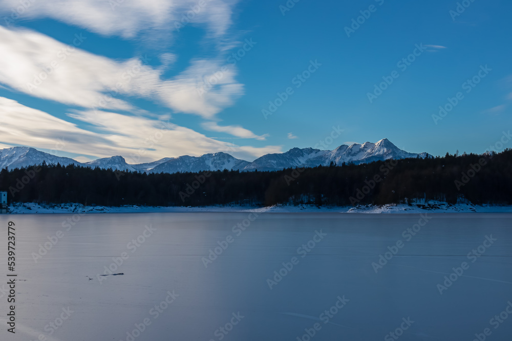Scenic view of frozen alpine lake Forstsee, Techelsberg, Carinthia (Kaernten), Austria, Europe. Breathing fresh cold air. Winter wonderland. Snow capped Karawanks mountain range, Mittagskogel (Kepa) Scenic view of frozen alpine lake Forstsee, Techelsberg, Carinthia (Kaernten), Austria, Europe. Breathing fresh cold air. Winter wonderland. Snow capped Karawanks mountain range, Mittagskogel (Kepa)