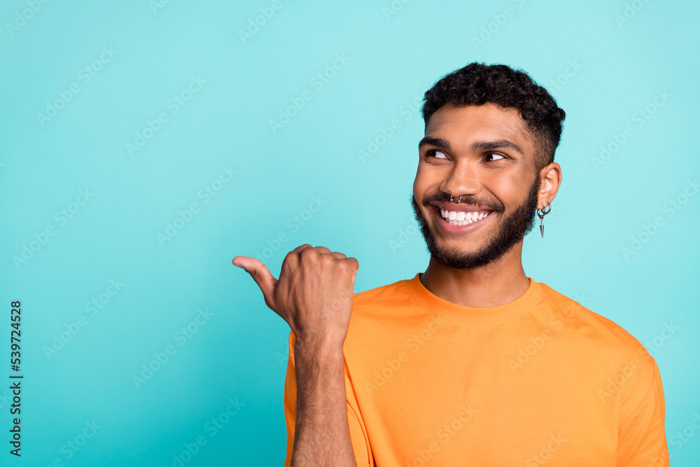 Photo of funky dreamy man dressed orange t-shirt looking pointing thumb empty space isolated turquoise color background Photo of funky dreamy man dressed orange t-shirt looking pointing thumb empty space isolated turquoise color background