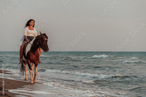 Woman in summer clothes enjoys riding a horse on a beautiful sandy beach at sunset. Selective focus 