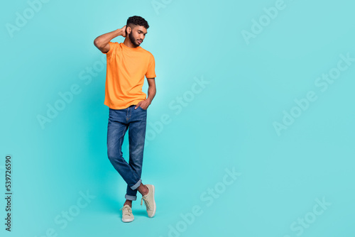 Full length photo of serious confident guy wear orange t-shirt arm head looking empty space isolated teal color background