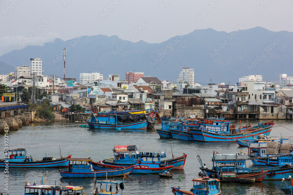 A skyline of the coastal Vietnamese town of Nha Trang with boats in the harbour and the hills beyond.