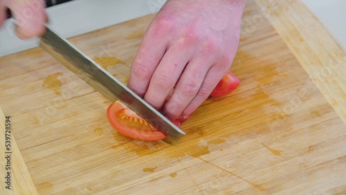 The hands of the cook cut tomatoes in the kitchen on the board close-up