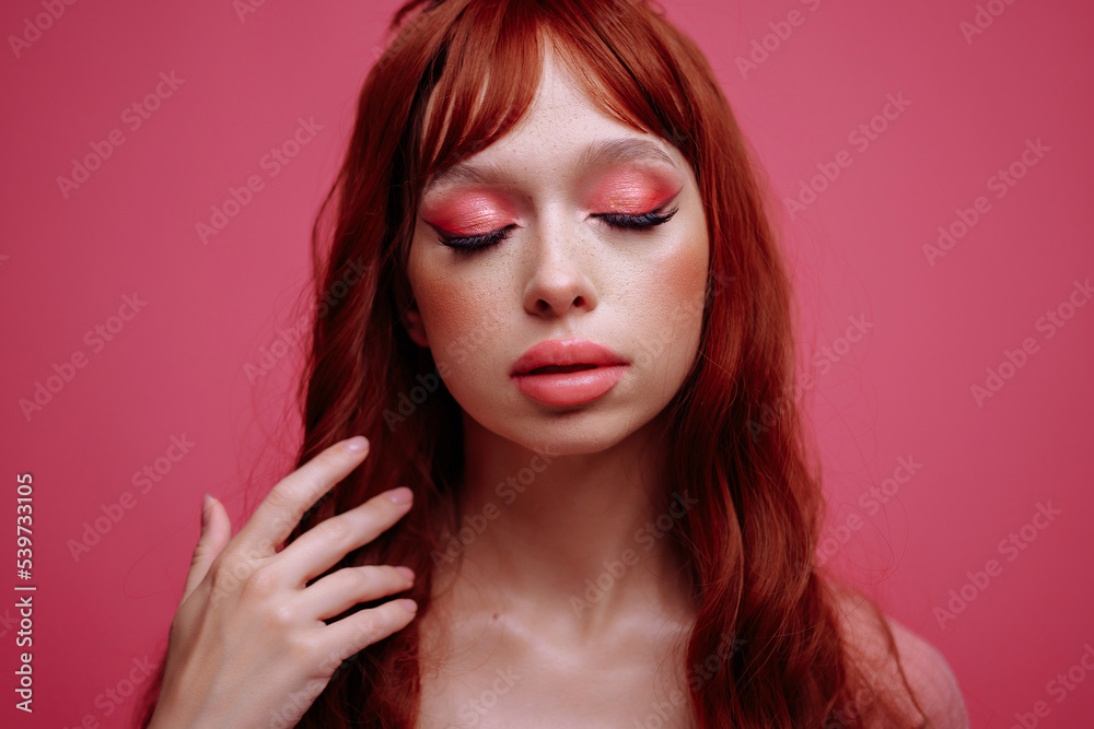  Beautiful young woman with red hair and bright pink makeup on a pink background