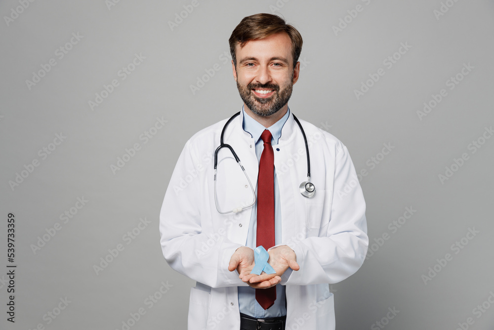 Male doctor man wears white medical gown suit work in hospital hold in hands blue ribbon aids symbol look camera isolated on plain grey color background studio portrait. Healthcare medicine concept. Male doctor man wears white medical gown suit work in hospital hold in hands blue ribbon aids symbol look camera isolated on plain grey color background studio portrait. Healthcare medicine concept.