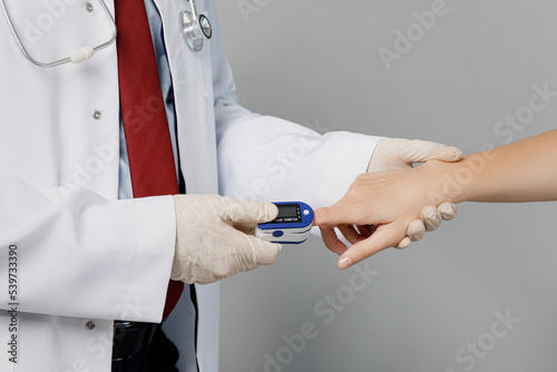 Cropped close up male doctor man wear white medical gown suit work in hospital use pulse oximeter apply on finger of patient isolated on plain grey color background studio Healthcare medicine concept