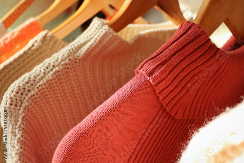 Warm sweaters on a wardrobe hanger on a light background. Autumn, winter clothes