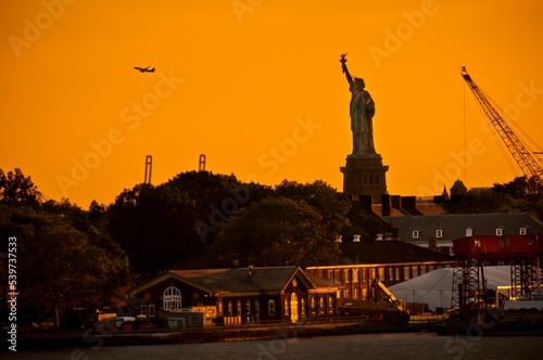 Statue of Liberty, buildings, and trees under the orange sunset sky