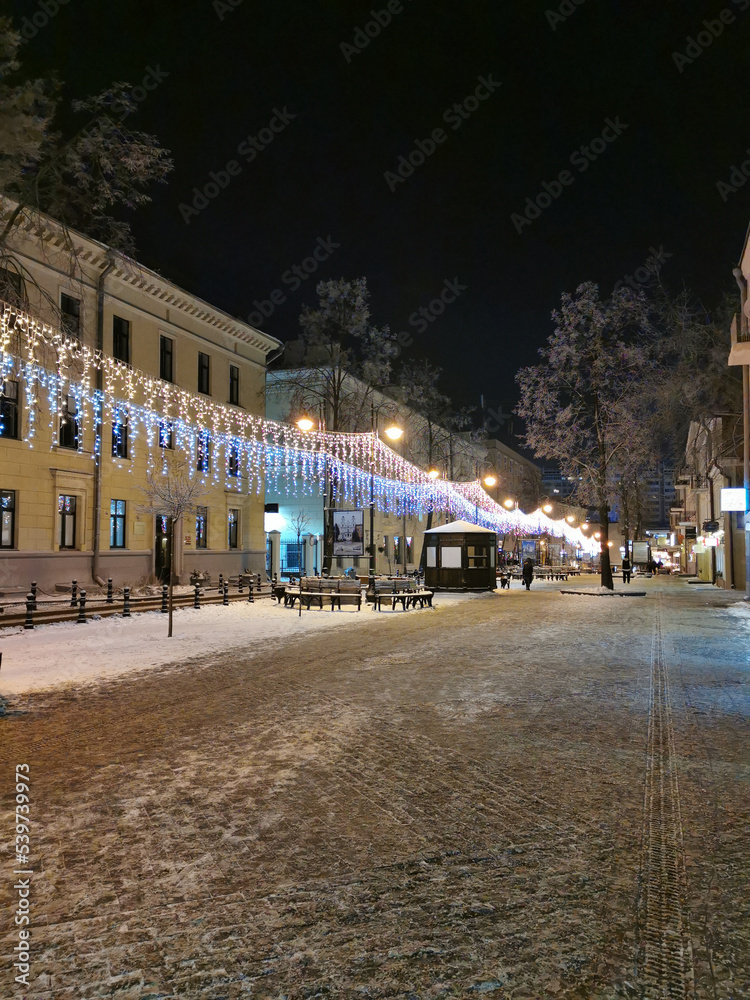 The evening street of the city in the snow is decorated with garlands for Christmas.