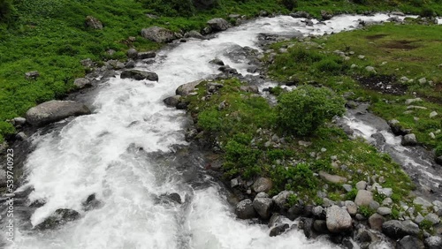 Stream water running through green valley.  Fast moving view from the drone on the river with rocky banks. Aerial top down shot 