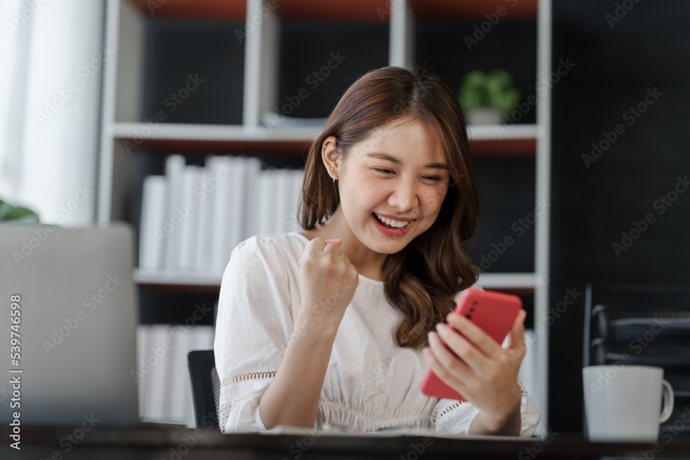 Pretty freelance asian business woman using mobile phone at working table in modern office.