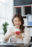 Pretty freelance asian business woman using mobile phone at working table in modern office.