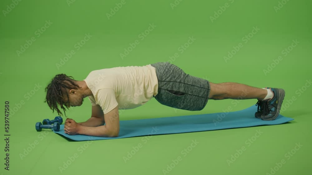 Young Man Making Plank Flexing Legs Exercise in Dynamic at Home. Sporty Fit Young Curly Mexican Man Doing Fitness Aerobic Exercises against Green Screen Background. Home Workout, Training and Wellness