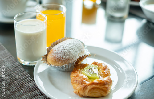 Croissant bread in a white plate with a glass of fresh milk and orange juice on the breakfast table.