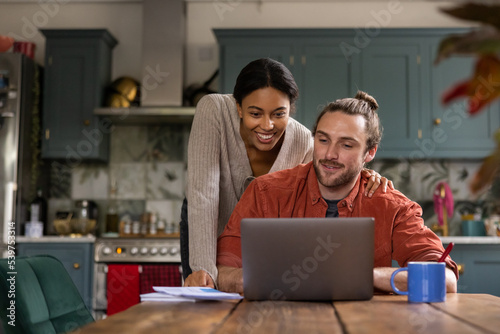 Happy young adult couple at home looking at personal finances using a laptop photo