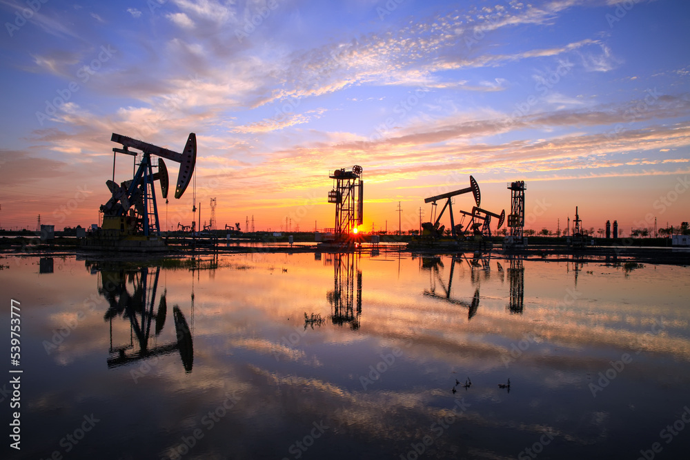 in the evening, oil pumps are running, The oil pump and the beautiful sunset reflected in the water, the silhouette of the beam pumping unit in the evening. in the evening, oil pumps are running, The oil pump and the beautiful sunset reflected in the water, the silhouette of the beam pumping unit in the evening.