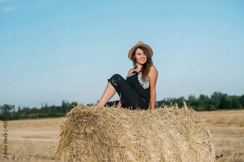 beautiful brunette woman in black overalls with a straw hat on a haystack in a field at sunset. High quality photo beautiful brunette woman in black overalls with a straw hat on a haystack in a field at sunset. High quality photo