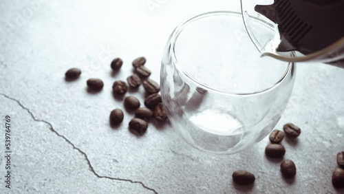 Pour hot black coffee into a mug and coffee beans on the table