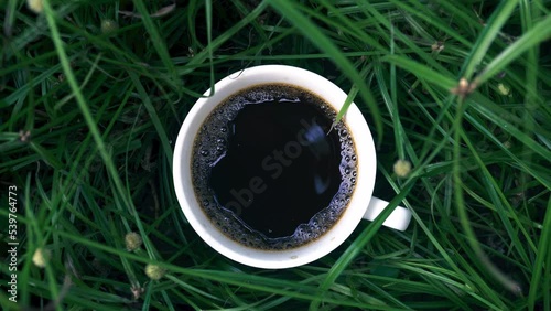Dark espresso coffee cup on the green grass, give a relaxing feeling