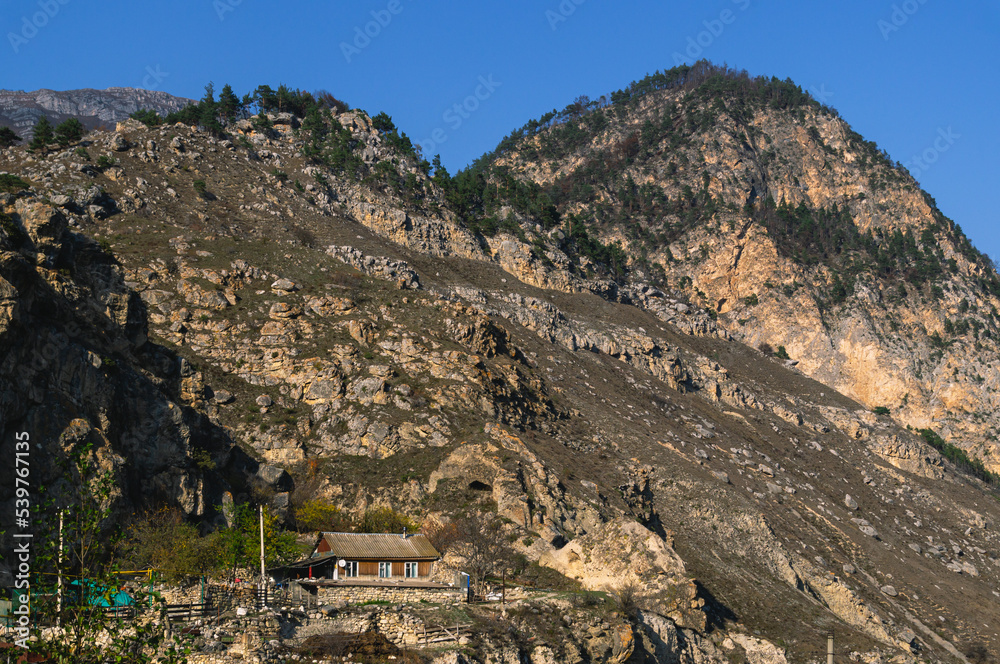 Autumn landscape in the mountains. Yellowed trees in autumn in the mountains of North Ossetia. Mountain gorges. View of the house high in the mountains. A village in the mountains.