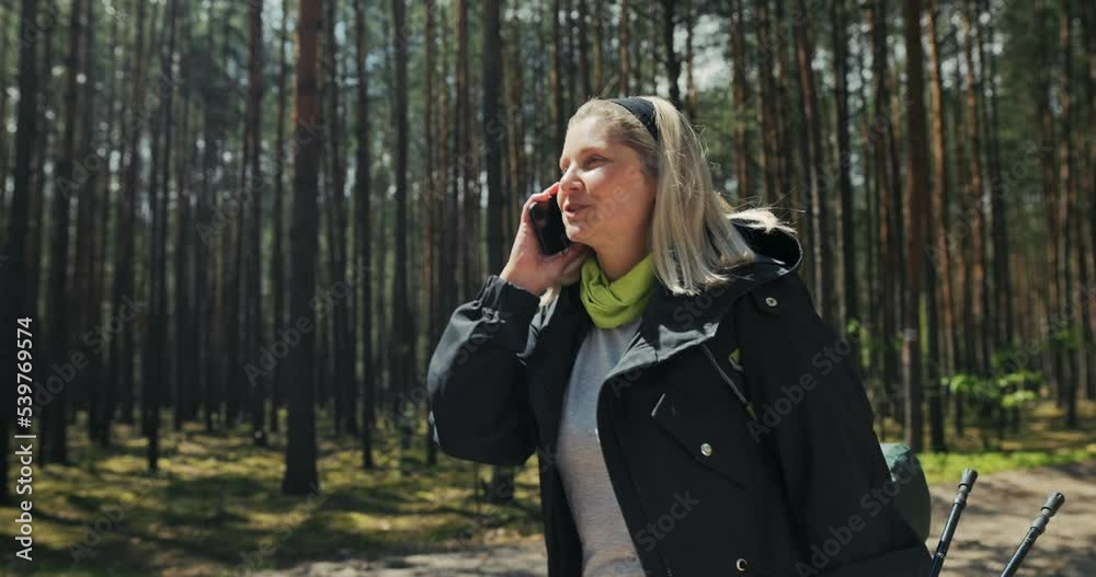Middle-aged woman with gray hair and headband wearing sports clothes stop in the middle of forest take out a fashionable phone of the latest series daughter calling . Middle-aged woman with gray hair and headband wearing sports clothes stop in the middle of forest take out a fashionable phone of the latest series daughter calling .