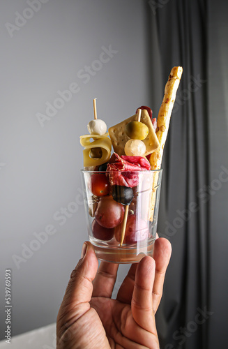 Man holds Jarcuterie in a glass, the modern version of charcuterie. includes various types of sausages, pickles and cheese photo