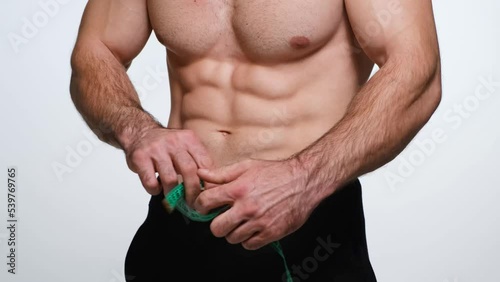 Strong bodybuilder measuring the width of his waist, putting a measuring tape over his abdomen, white background