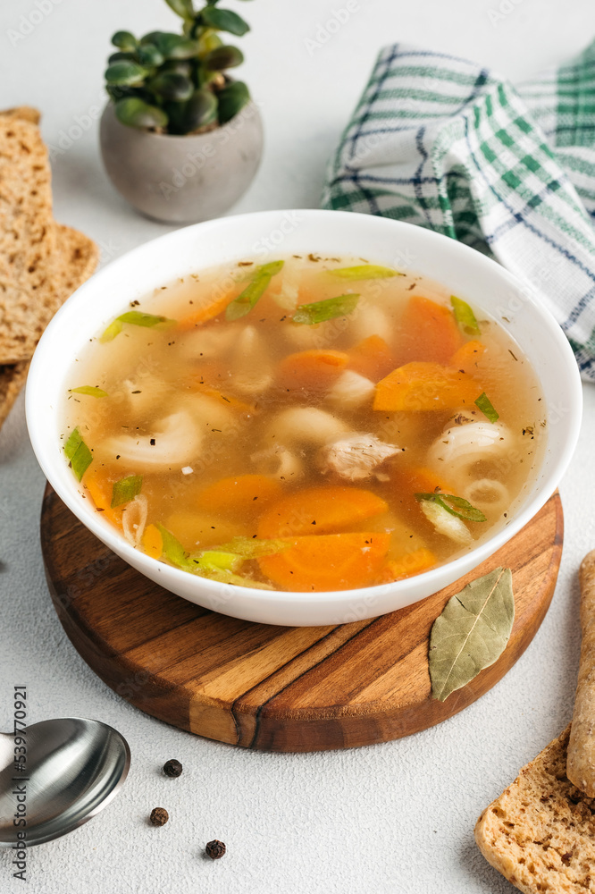 chicken soup broth with vegetables in a white bowl, next to a spoon, bread, towel, spices
chicken soup broth with vegetables in a white bowl, next to a spoon, bread, towel, spices