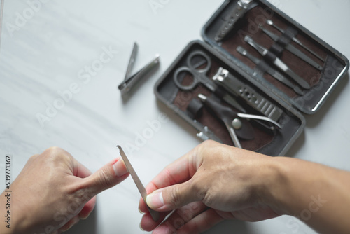 Billede på lærred Holding hand cutting nails manicure and pedicure tool set concept, cosmetic accessories for nails, scissors, pusher cuticle and nail file, cleaning nails for protection dirt bacteria in nails