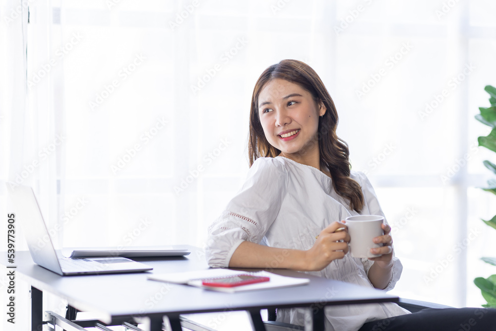 Beautiful young smiling asian woman working on laptop and drinking coffee in at workplace, Asia business woman working document finance and calculator in her home office. Enjoying time at home. Beautiful young smiling asian woman working on laptop and drinking coffee in at workplace, Asia business woman working document finance and calculator in her home office. Enjoying time at home.