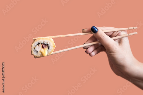 A hand holds a fried sushi roll with cheese with wooden sticks
