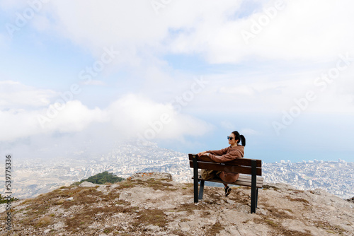 Happy traveler in sunglasses enjoys a beautiful view of the sea, a young man sits on a bench and looks into the distance. The concept of freedom, vacation, vacation and summer travel