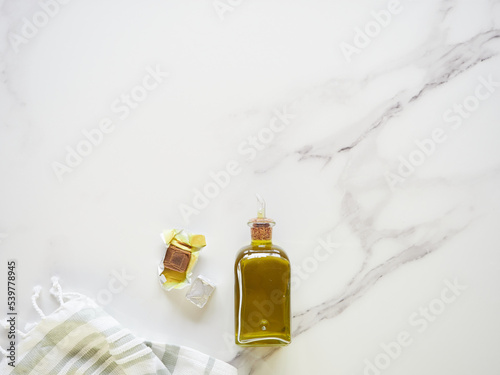 small glass bottle with olive oil, unwrapped stock cube and tea towel on white marble kitchen counter, top view with copy space.