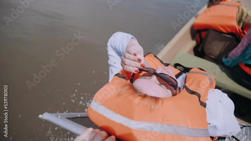 A woman in Life jacket enjoys traveling while sailing on a motor boat on the river. Elderly tourism. Happy tourist.  photo